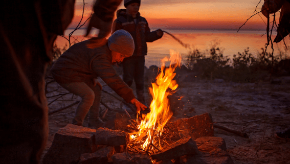 Eine Familie spielt gemeinsam am Lagerfeuer und verbringt Zeit in der Natur – ein Moment, der zeigt, wie man regenerativ leben kann